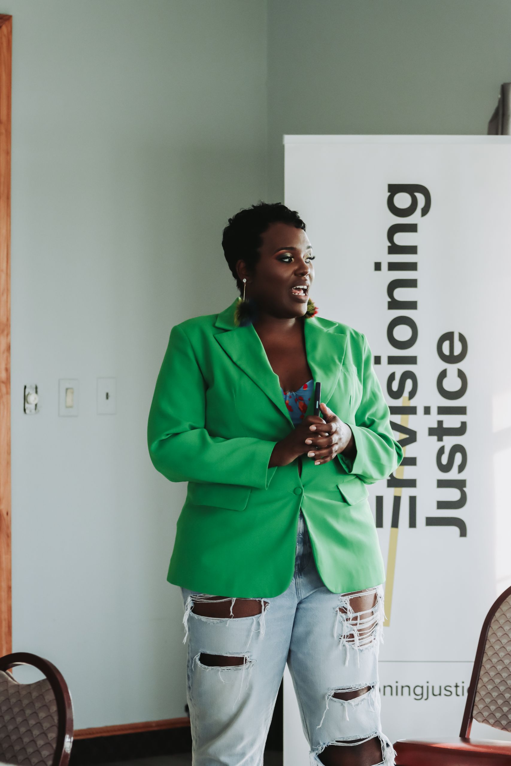 Amplifying Diverse Voices: The Importance of Inclusive Leadership - Confident woman in green blazer presenting at social justice event.