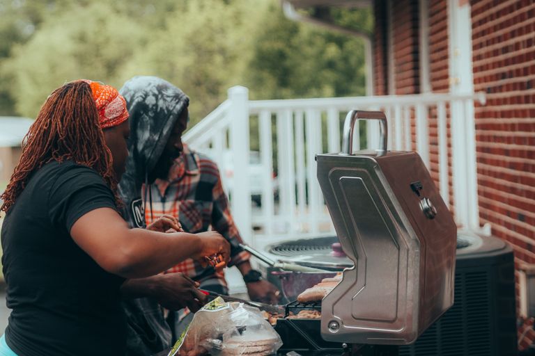 Backyard BBQ Really Means in a Black Family -Two adults grilling sausages on a backyard barbecue grill. Perfect family leisure activity.