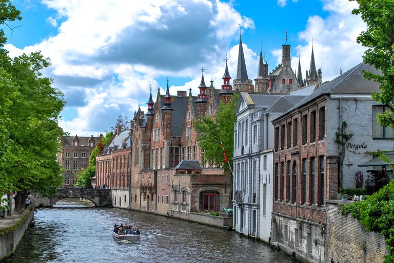 Belgium Travel Guide - Charming canal scene in Brugge, Belgium showcasing historic architecture and a tour boat on a sunny day.