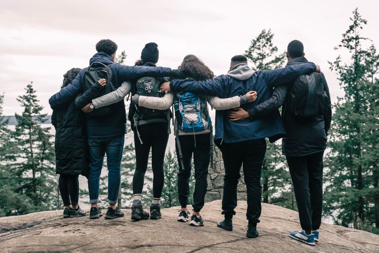 Belonging Begins Where Performance Ends - A diverse group of friends hiking and embracing at a scenic outdoor viewpoint.