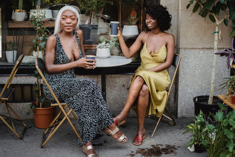 Black Women Deserve a Life With Room to Exhale - Two women sit together, enjoying coffee at an outdoor café amidst greenery.