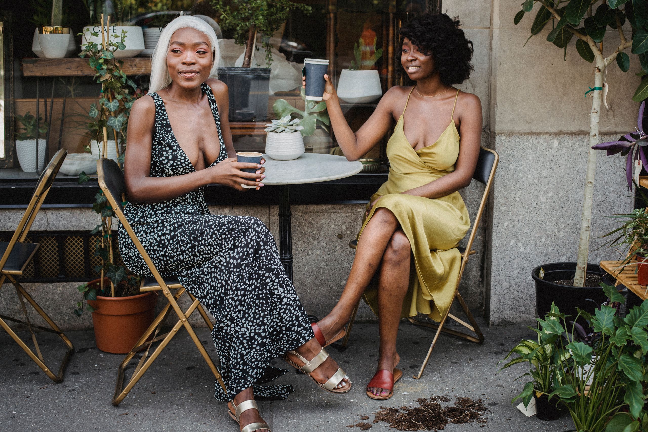 Black Women Deserve a Life With Room to Exhale - Two women sit together, enjoying coffee at an outdoor café amidst greenery.