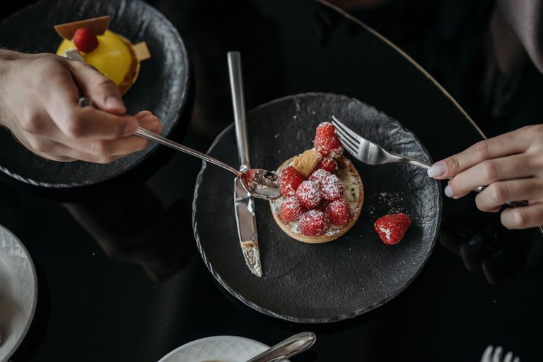 Close-up of a raspberry tart with powdered sugar on a black plate, top view. - Close-up of a raspberry tart with powdered sugar on a black plate, top view.