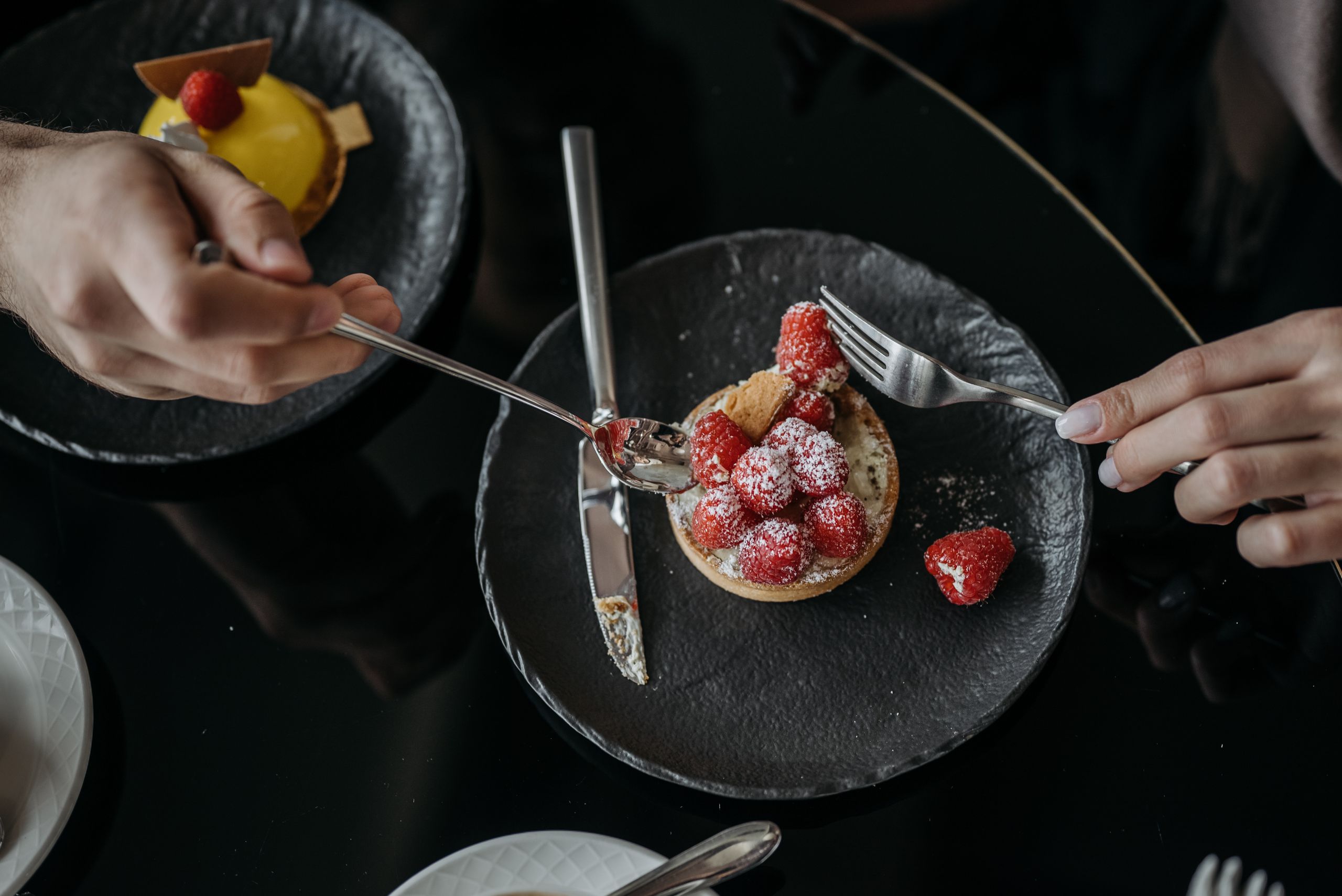 Close-up of a raspberry tart with powdered sugar on a black plate, top view. - Close-up of a raspberry tart with powdered sugar on a black plate, top view.