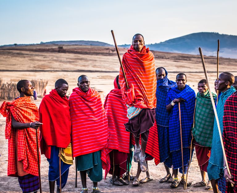 Cultural Travel Requires Humility - A group of Maasai men in vibrant traditional attire performing a cultural jumping dance outdoors.