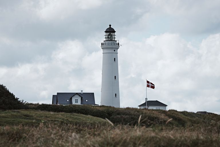 Denmark Travel Guide - A scenic view of Hirtshals Lighthouse, Denmark, with a Danish flag, captured on a cloudy day.