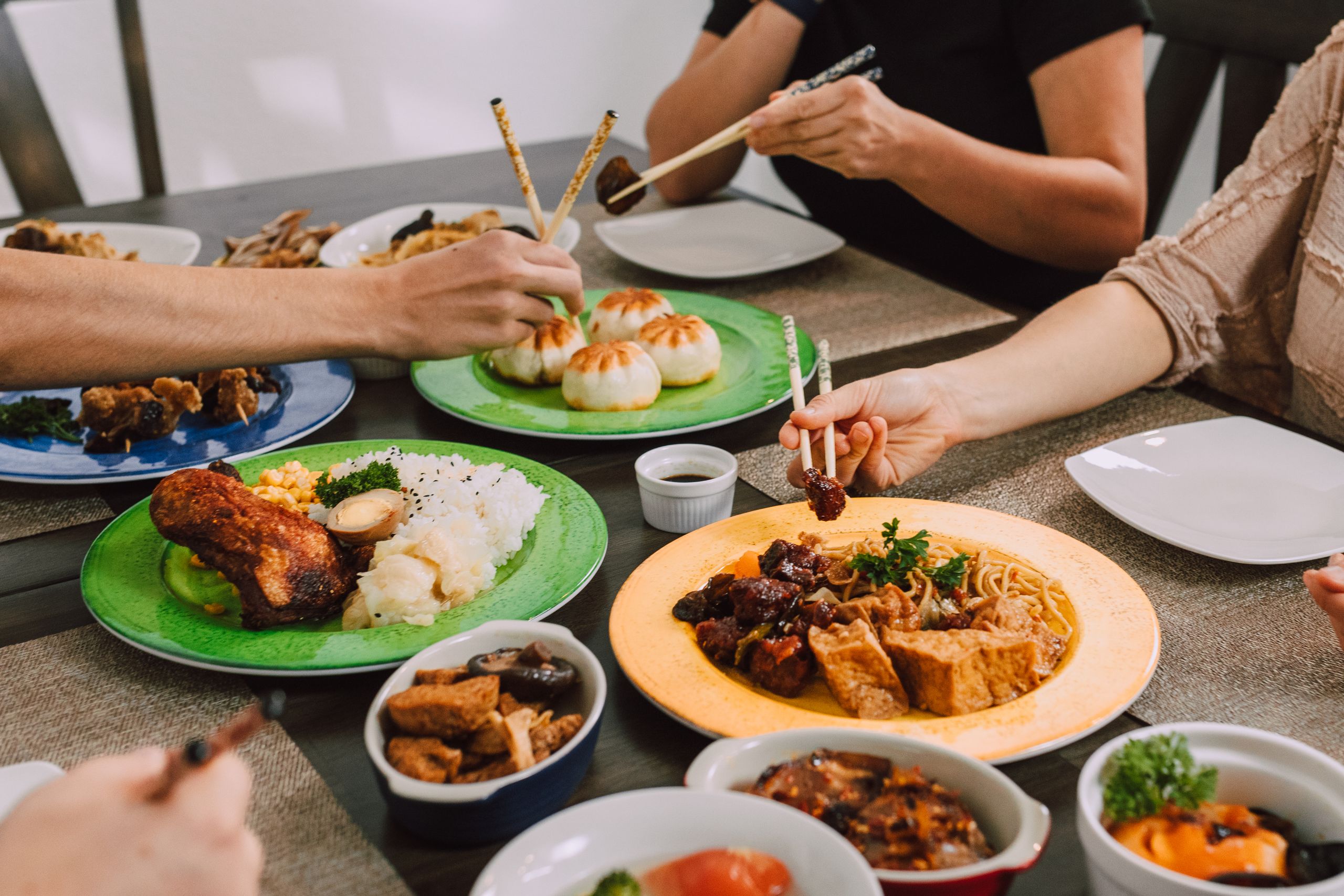 Diners enjoy a variety of Asian dishes including buns, noodles, and rice at a shared table.