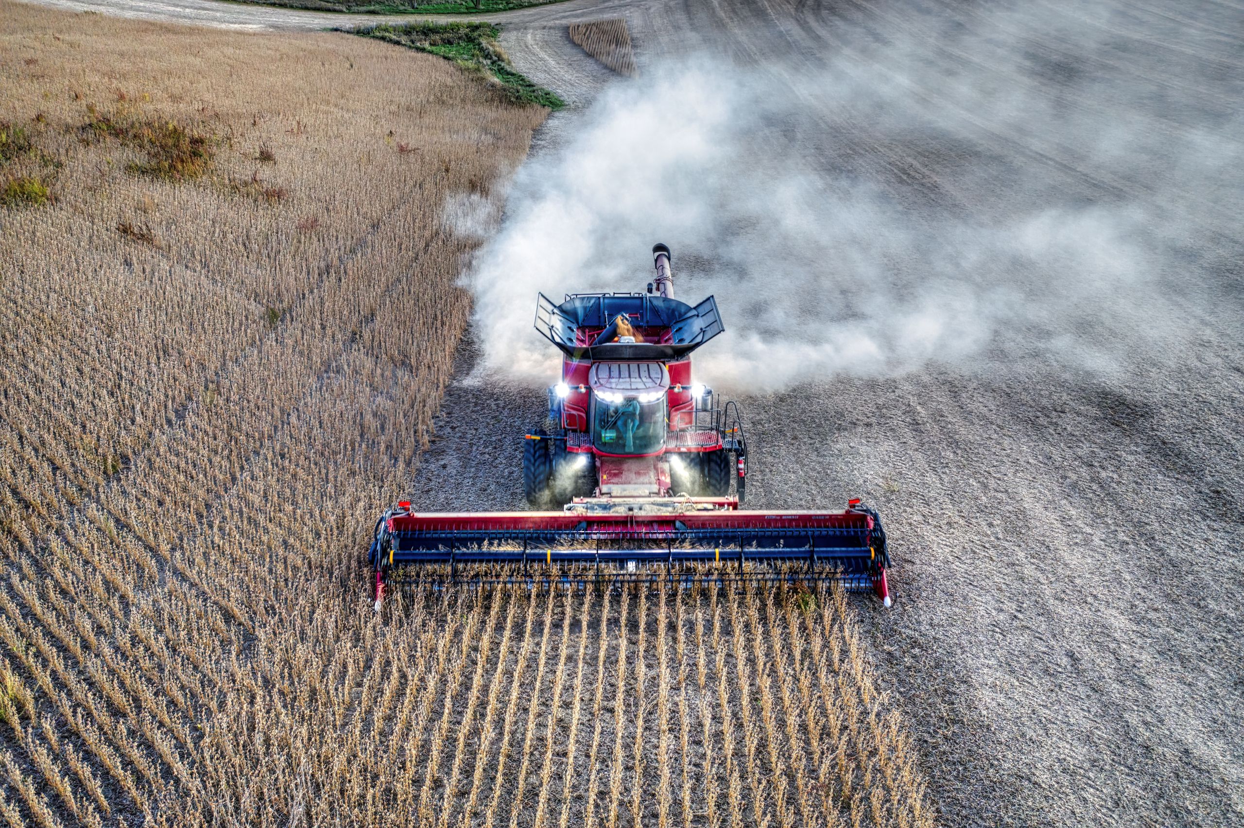 Drone photo of a red tractor harvesting soybeans in Minnesota farmland at day. - Precision Agriculture