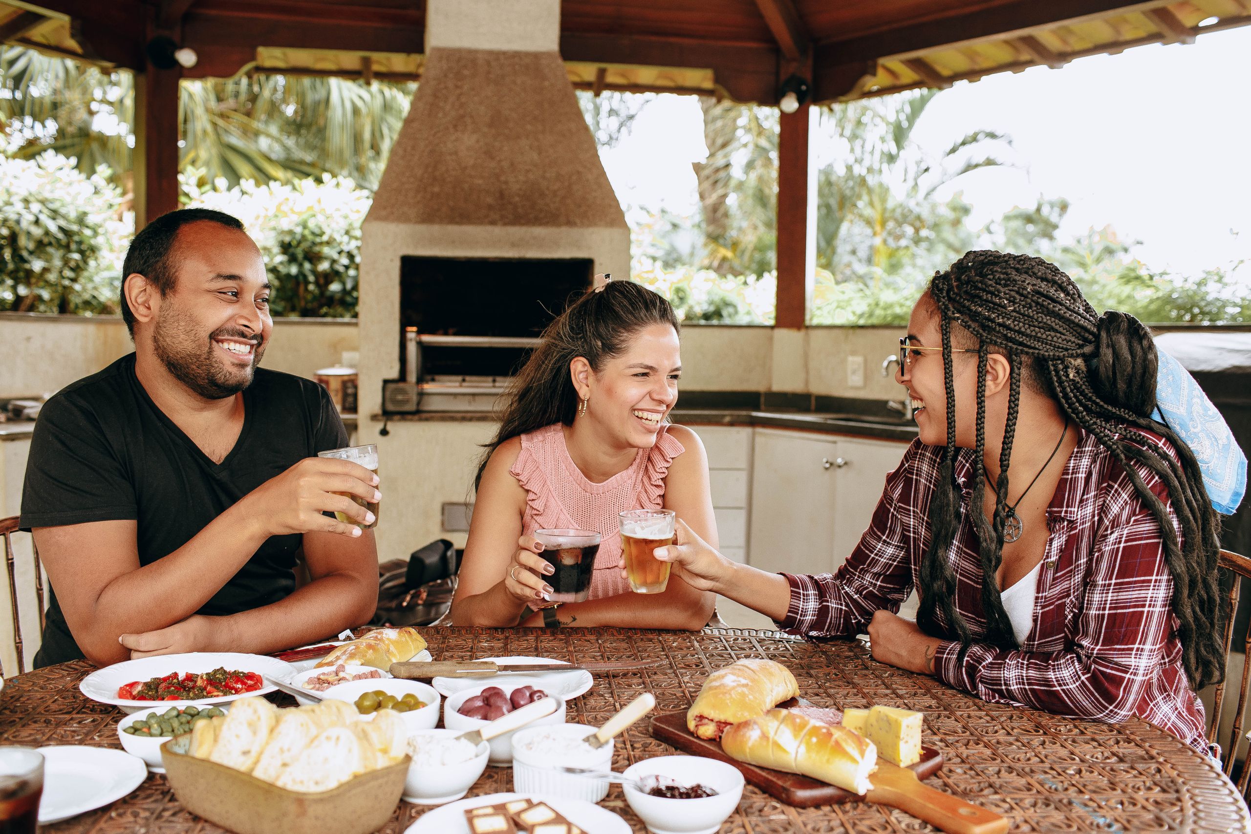 Everything the Kitchen Table Has Been Asked to Carry - Three friends sharing a joyful meal outdoors, enhancing camaraderie and togetherness.