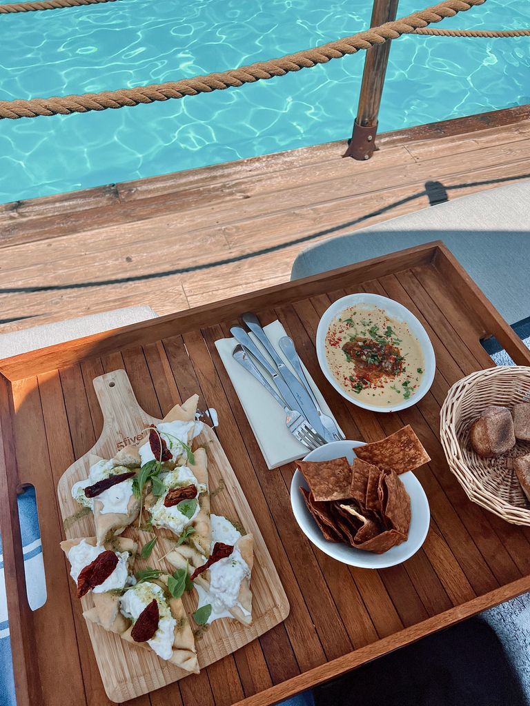 Food Tastes Better Near Water - Wooden tray with Mediterranean snacks poolside, ideal for summer relaxation.