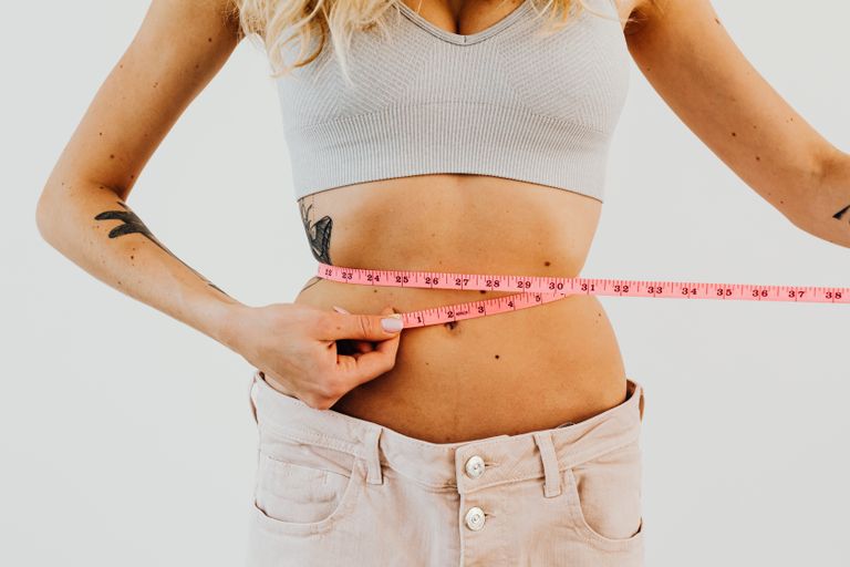 Fusion Burn Weight Loss Supplement Review | DG Speaks - Close-up of woman in sports bra measuring waist with pink tape for fitness goals.