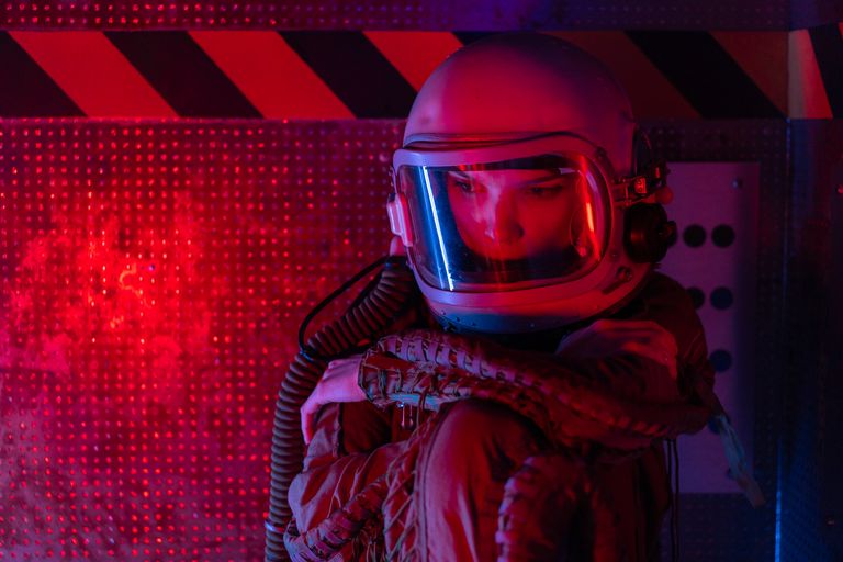 Gender Portrayal in Sci-Fi Films - Astronaut in space suit sitting thoughtfully in red futuristic setting.