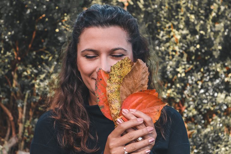 Gratitude - A woman enjoys the scents of colorful autumn leaves outdoors.