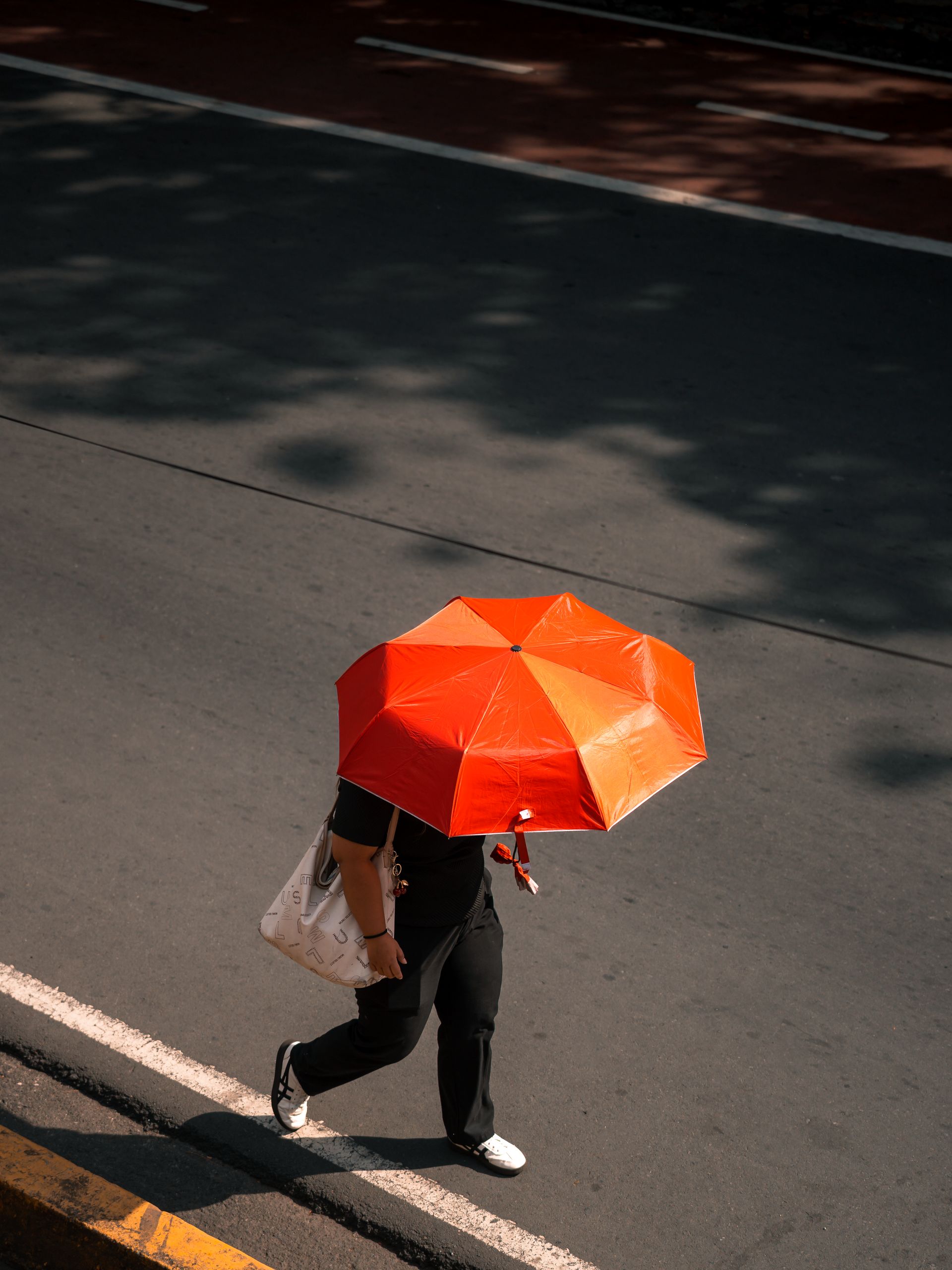 Summer Heat Reveals a City’s Design - High angle view of a person walking on a sunny day with a red umbrella along a street in Manila, Philippines.