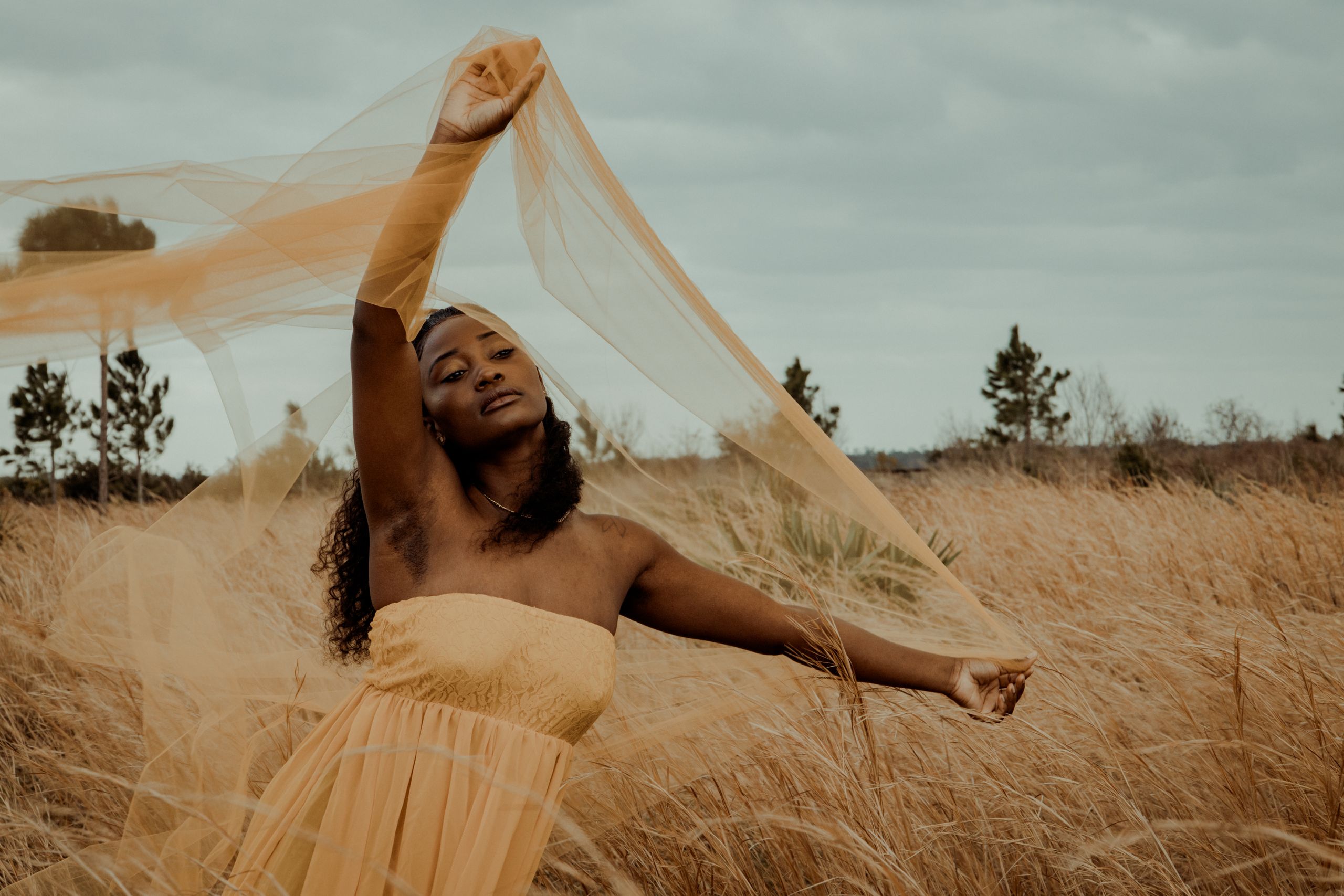Honoring the Woman I Am Becoming - Woman posing in a flowing yellow dress amidst tall grass, creating a serene and elegant outdoor portrait.