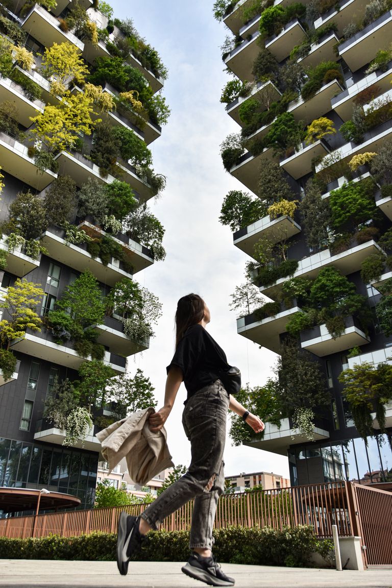 I Want a Sustainable Life, Not an Impressive One - Woman walking beneath eco-friendly buildings with lush vertical gardens.