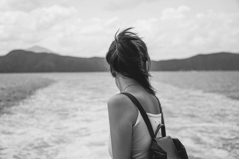 I Want Travel That Leaves Me More Human - A woman in a tank top stands on a boat looking at the sea, capturing the essence of travel and contemplation.