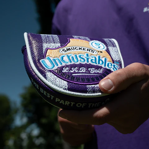 Limited-edition purple L.A.B. Golf x Uncrustables putter headcover inspired by Uncrustables sandwich packaging.