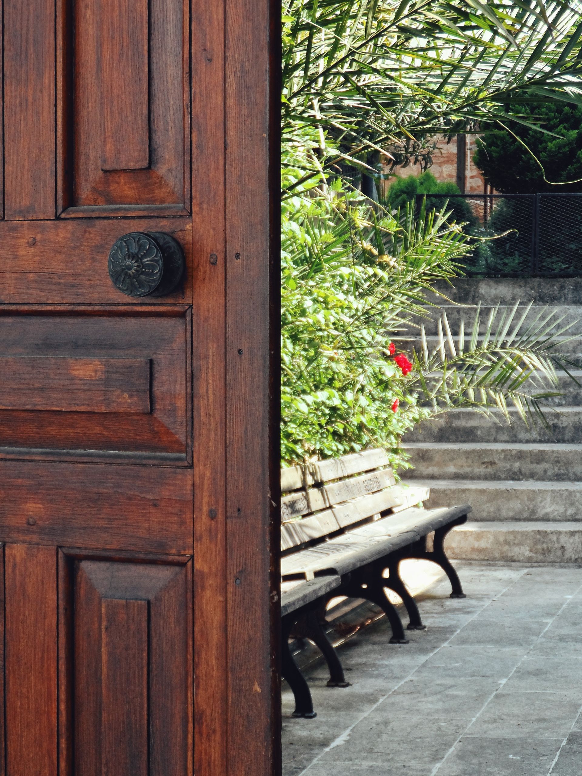 More Open Doors - A rustic wooden door opens to a peaceful garden with benches and lush greenery.