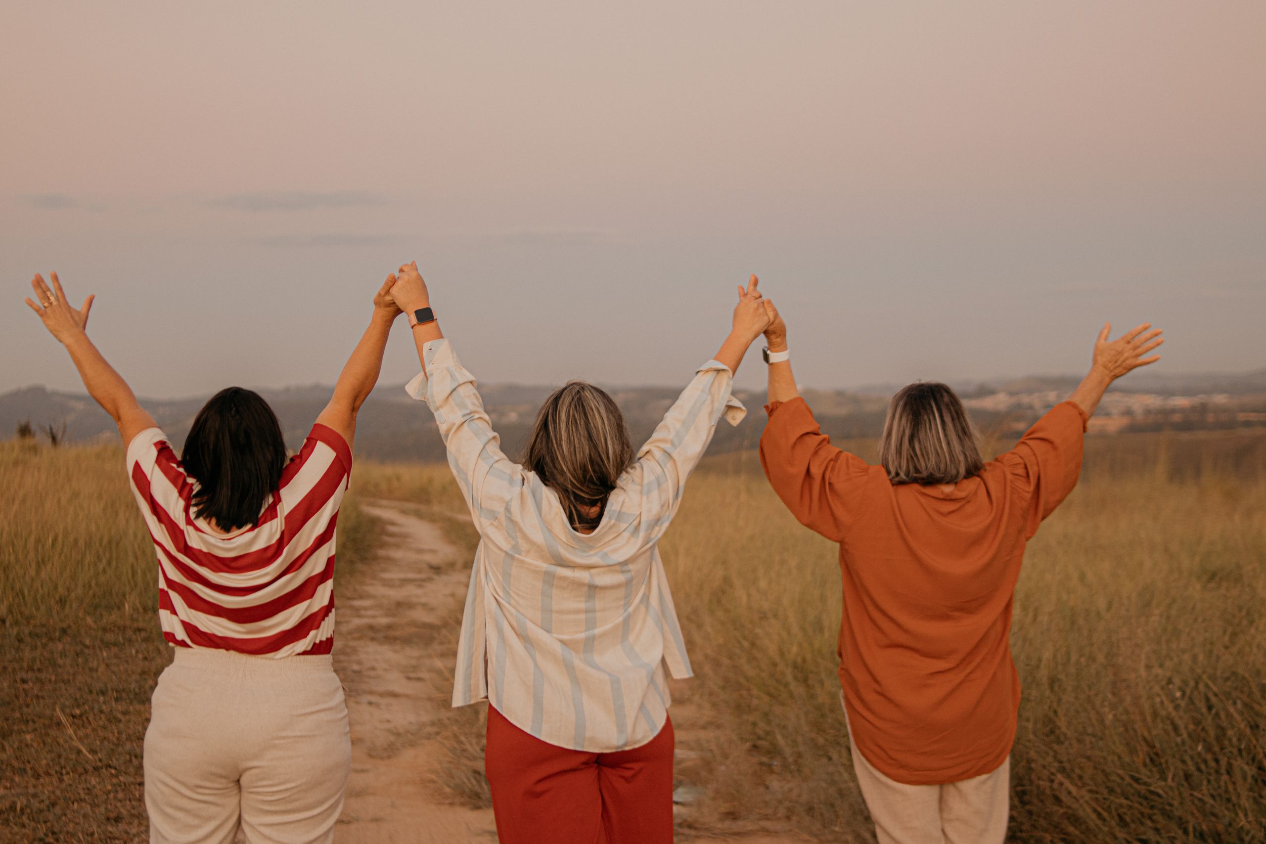 National Women Support Women Day - Three women standing in a São Paulo field, holding hands and raising arms, celebrating friendship.