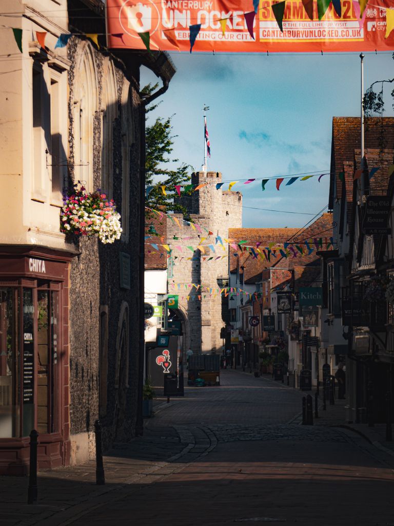 Scenic street in Canterbury featuring colorful bunting and historic stone tower.