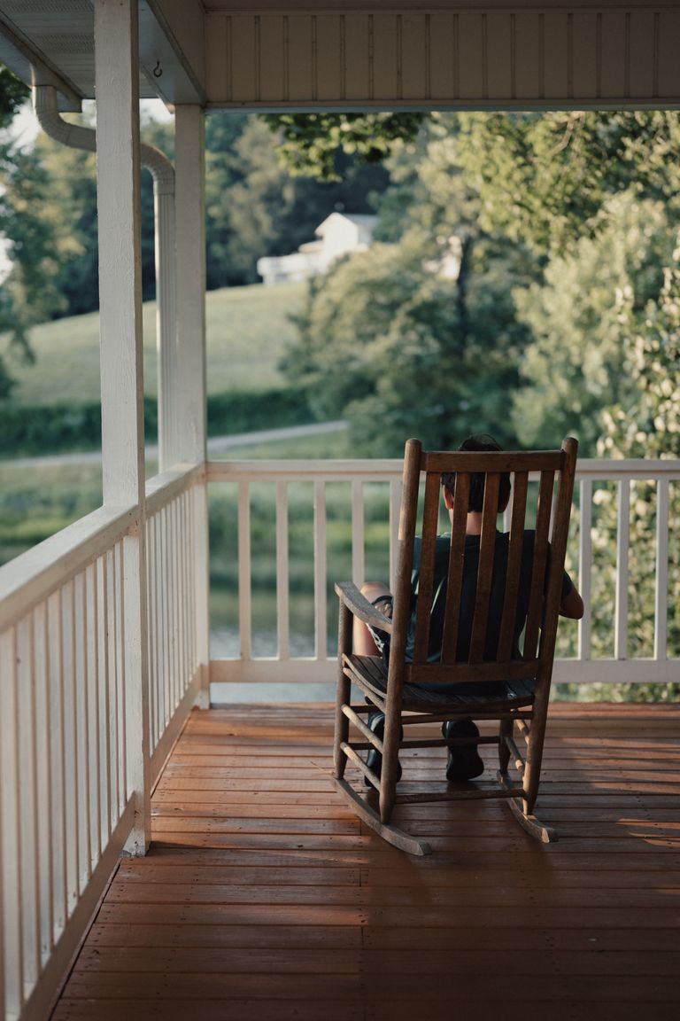 Softer Ambition Lets Me Build Without Losing Myself - A serene view from a country porch with a cozy wooden rocking chair overlooking the countryside.