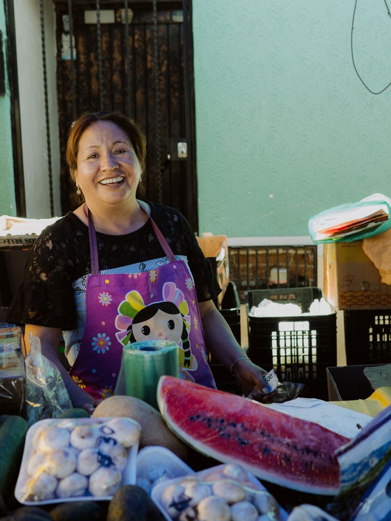 Somebody Fed Us: Honoring the People Behind Every Meal - Smiling woman selling fresh fruits at a bustling market in San Juan del Río, Mexico.