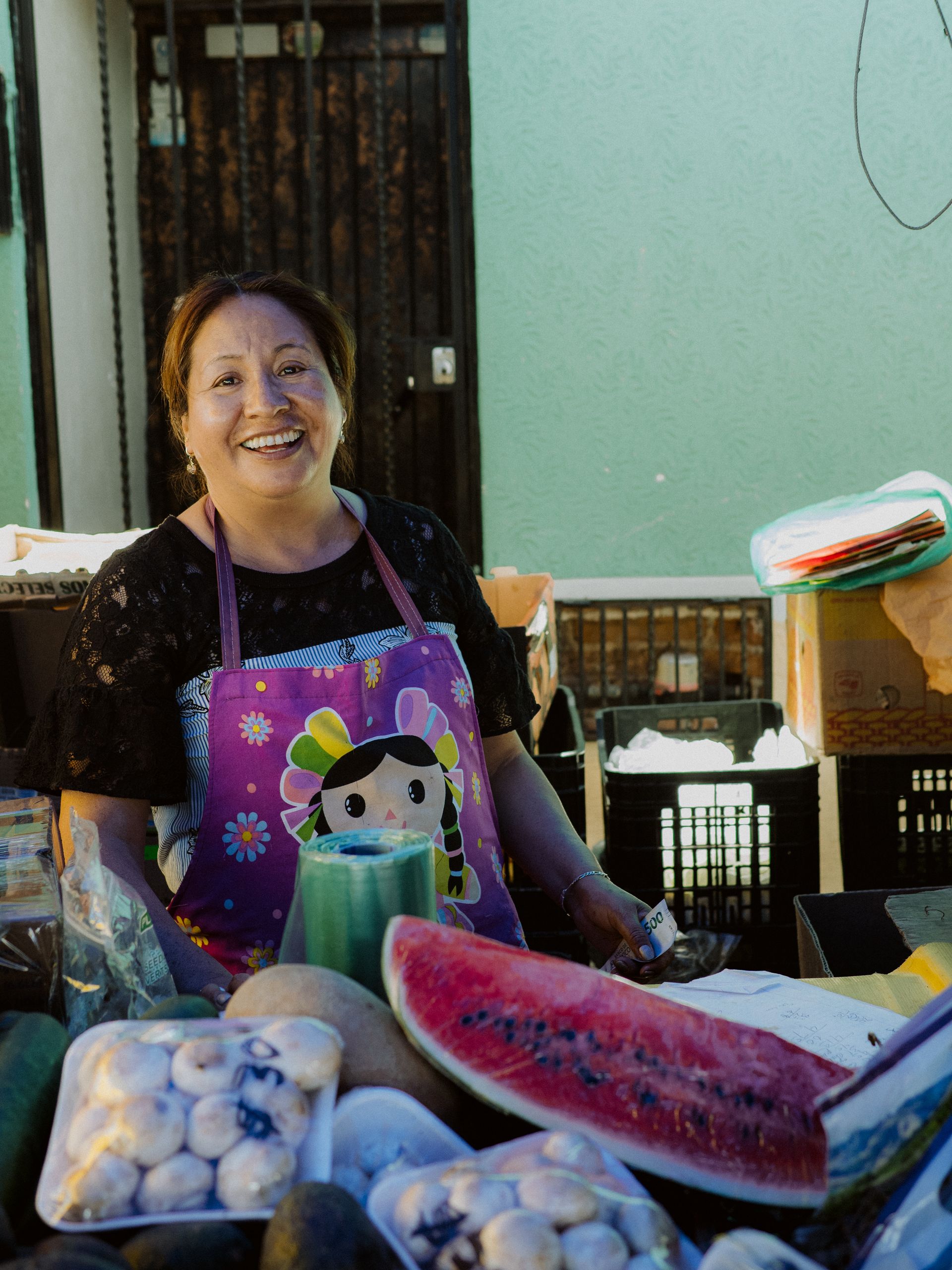 Somebody Fed Us: Honoring the People Behind Every Meal - Smiling woman selling fresh fruits at a bustling market in San Juan del Río, Mexico.