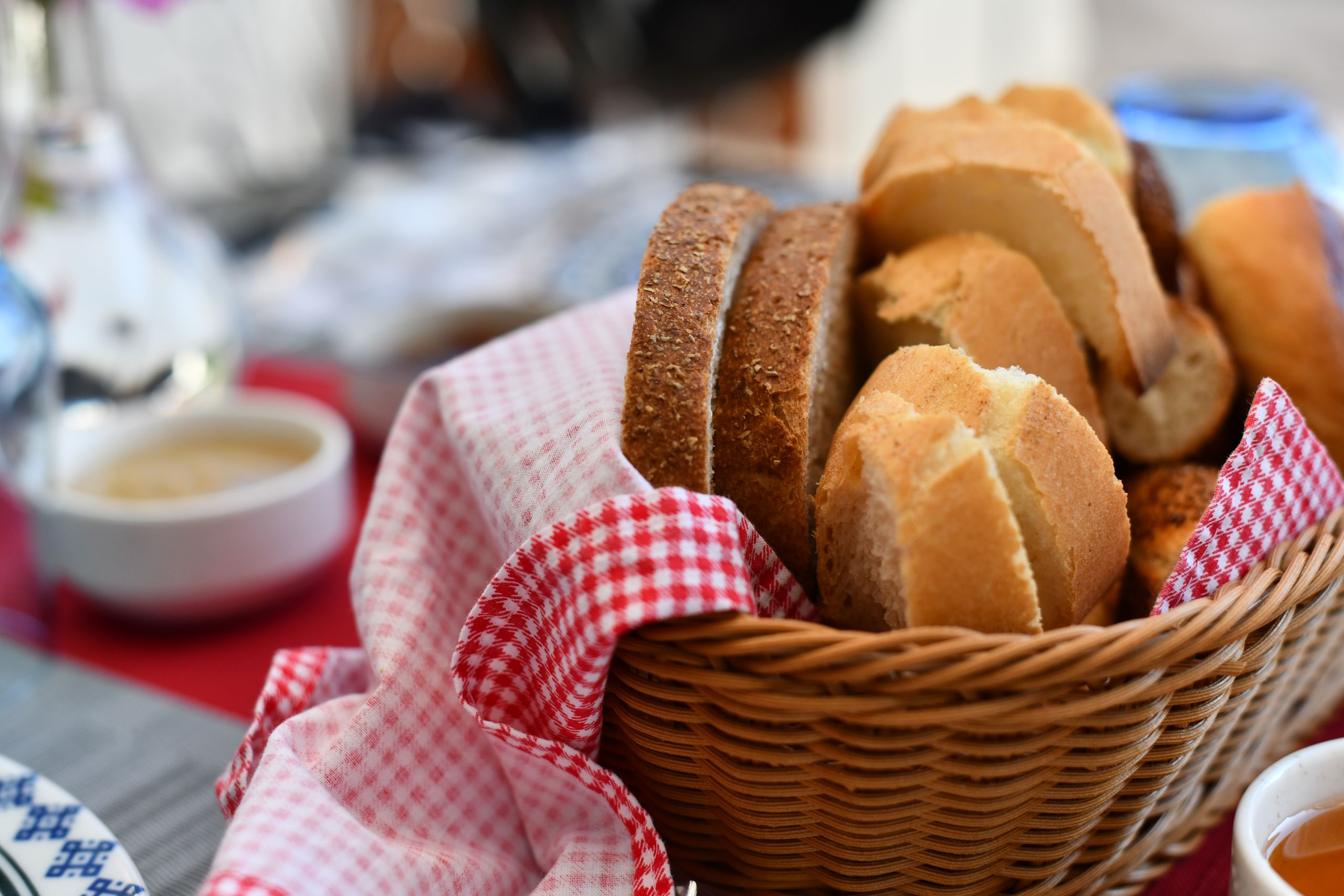 Sometimes Welcome Arrives in a Bread Basket - Assorted bread rolls in a wicker basket with red gingham cloth, perfect for breakfast.