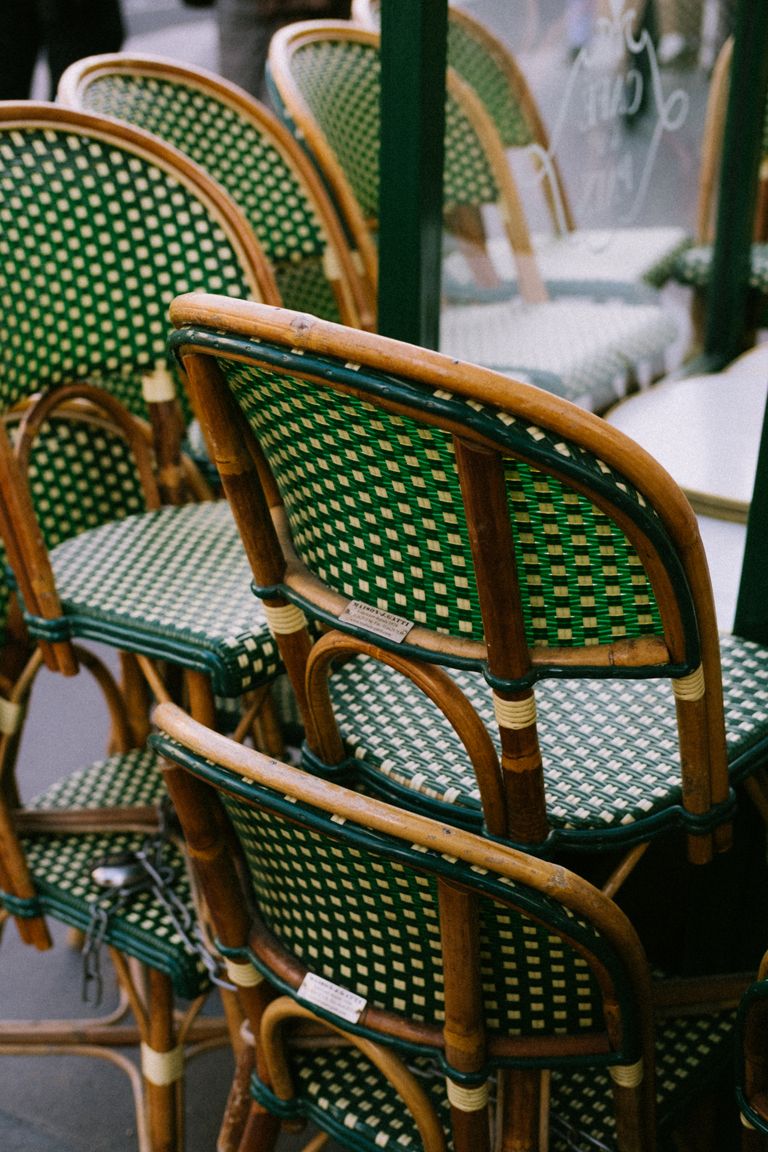 The Comfort of a Familiar Café Chair - Stacked rattan chairs with green checkered pattern in a classic outdoor café setup.