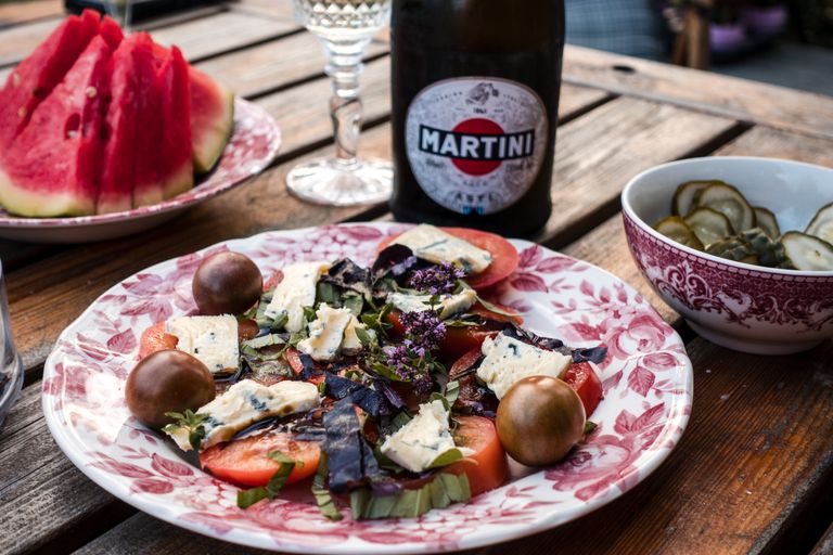 Summer meal - Vibrant garden salad with cheese, surrounded by watermelon, pickles, and wine on a rustic table.