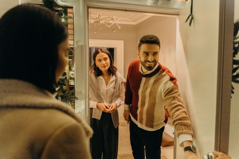 The Art of Hosting While Living On-Site - A couple greeting a guest at their doorway, capturing the warmth of a home during the holiday season.