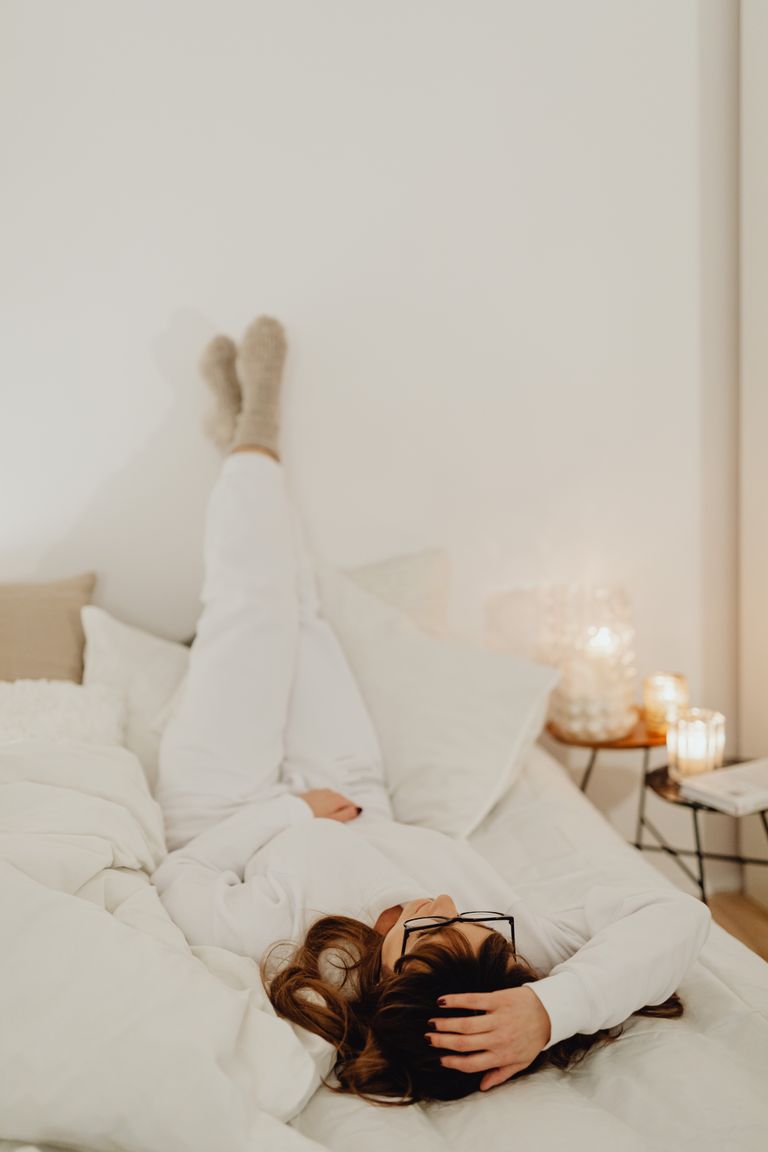 The Courage of Making a New Room for Yourself - Woman relaxing in a cozy, minimalist bedroom setting with warm lighting and soft textures.