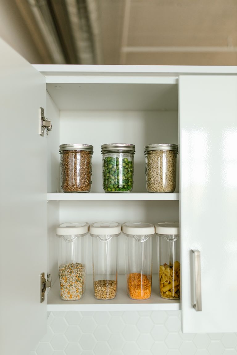 The Foods We Save for Hard Days - Neatly organized kitchen cabinet with various food items in jars and containers on shelves.