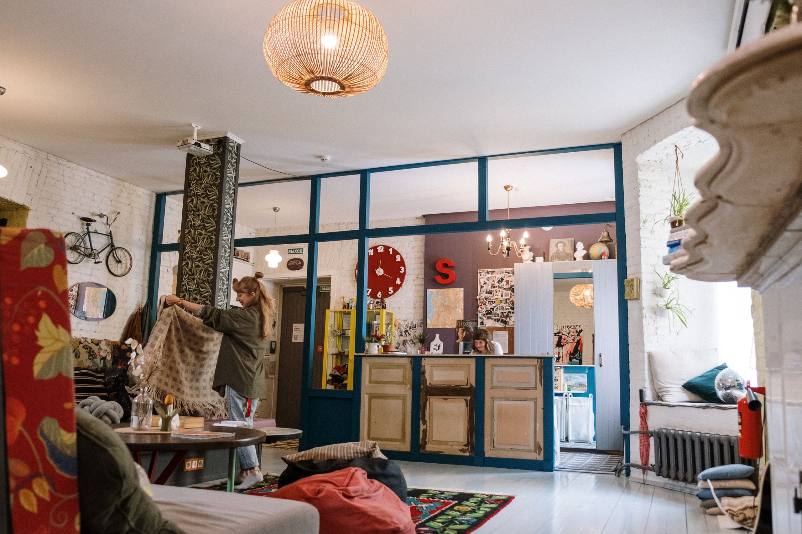 The Hospitality Lessons Hidden in Hostels - A vibrant living room with eclectic furnishings and a person arranging fabric, creating a cozy atmosphere.