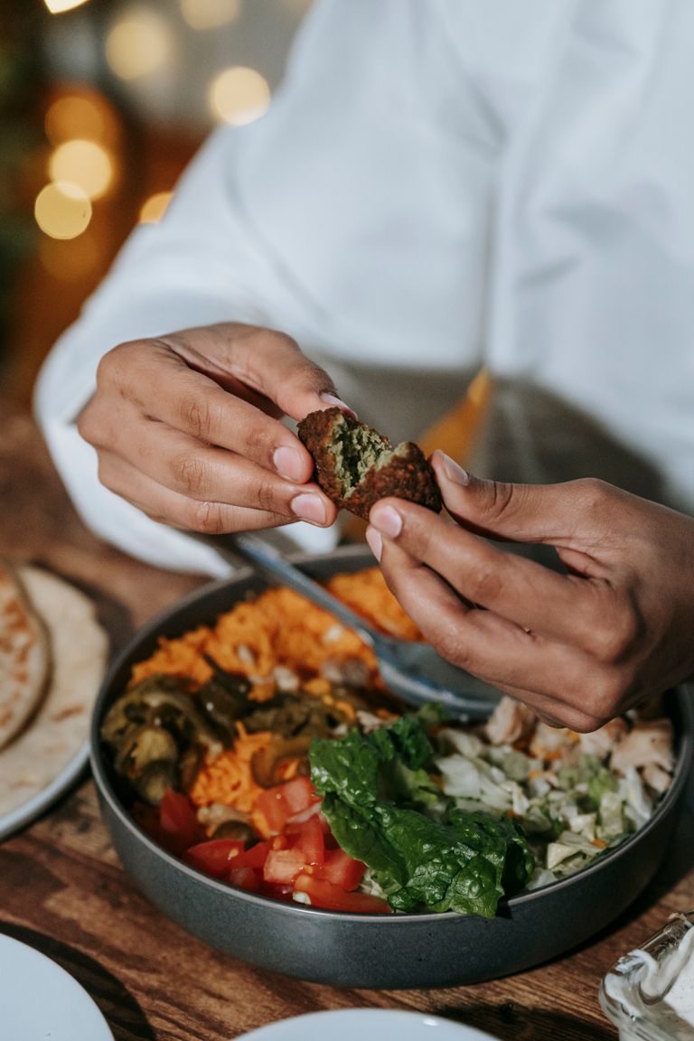 The Joy of Eating With My Hands - Hands breaking a falafel over a delicious plate of vegetables and salad, creating a healthy meal.