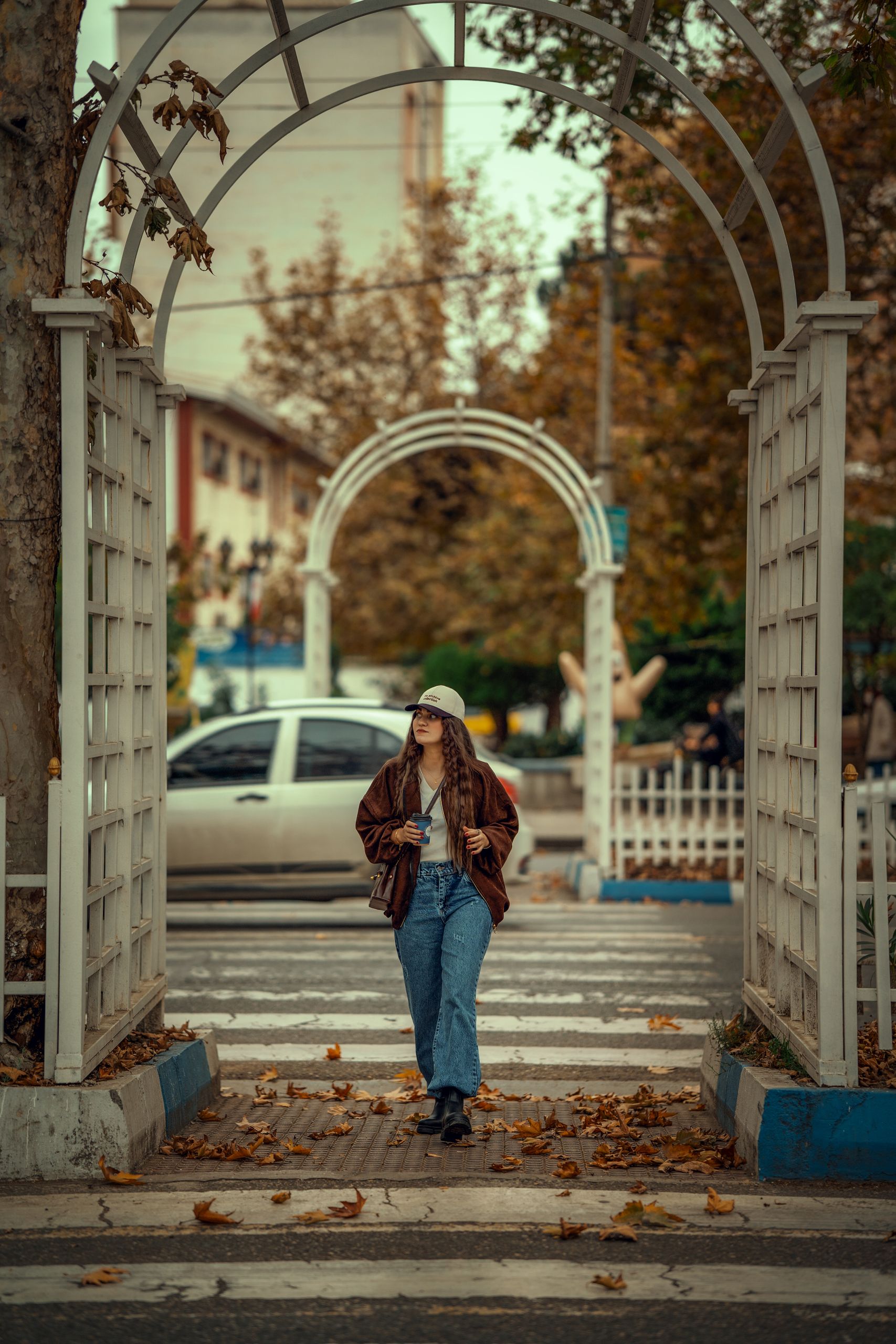 The Long Walk That Clears the Noise - A fashionable woman walks through a leafy street archway in fall attire.