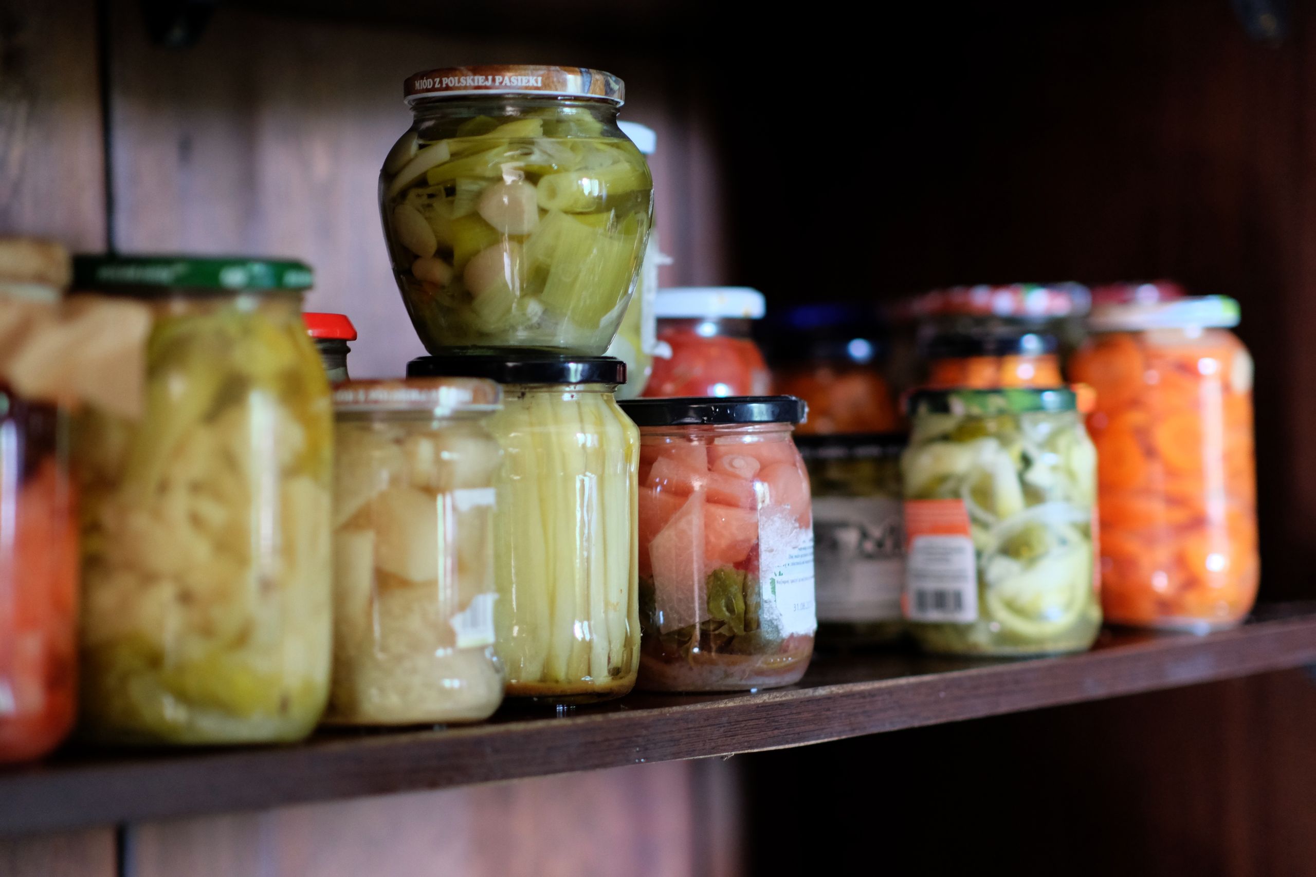 The Pantry Is a Quiet Kind of Security - A variety of colorful preserved vegetables in jars arranged on a wooden shelf.