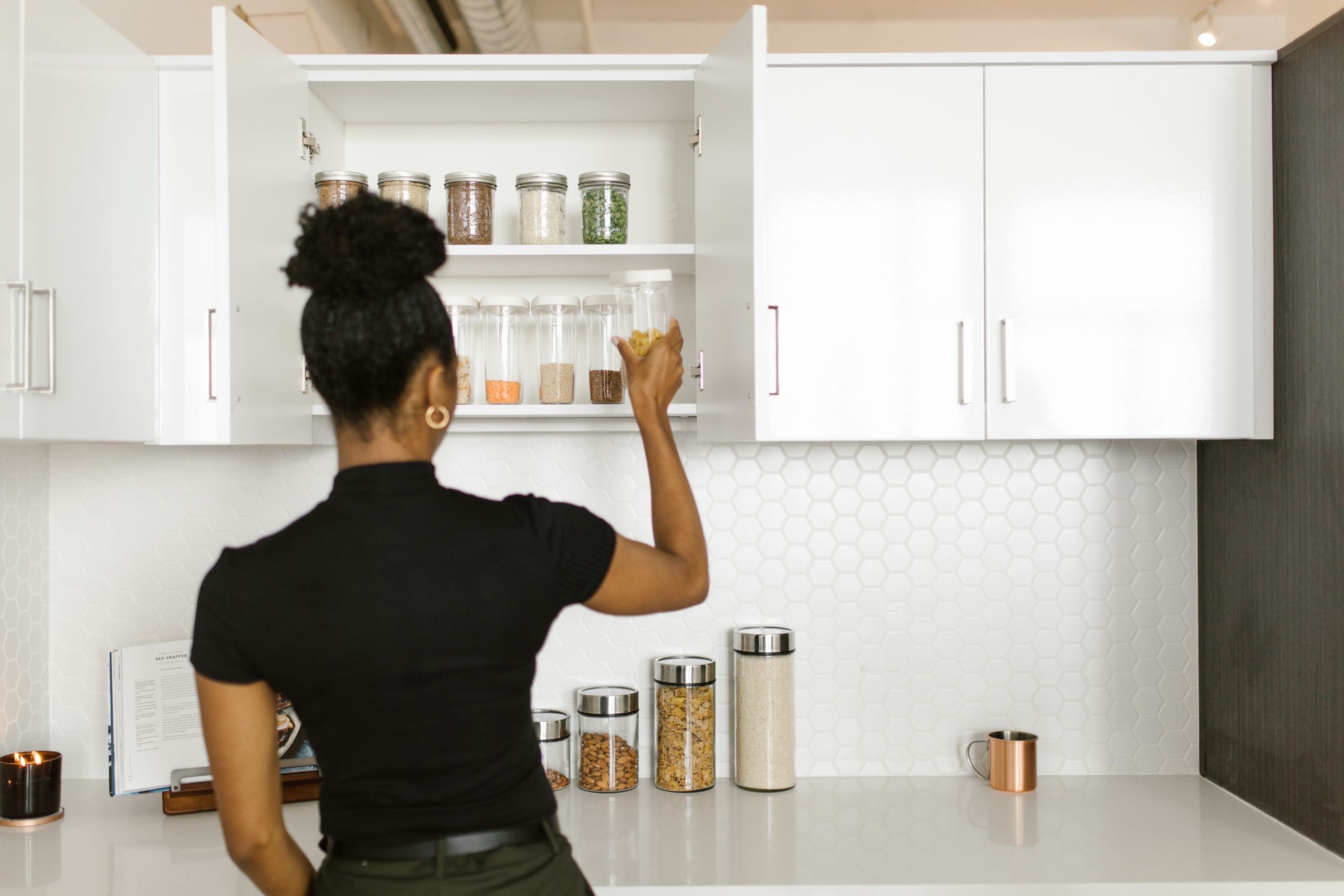 The Pantry Meal That Saves the Evening - A woman organizing a pantry shelf with various food jars in a modern kitchen.