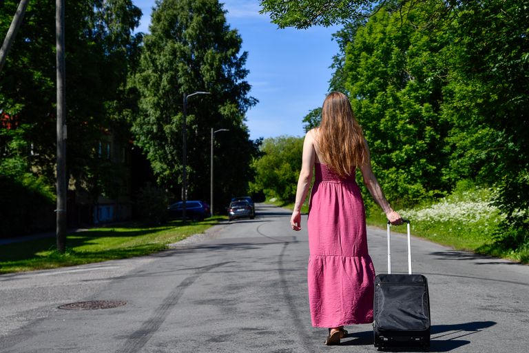 The Power of a Woman Walking Away - A woman in a pink dress walks down a sunny street in Tallinn, Estonia, pulling a suitcase.