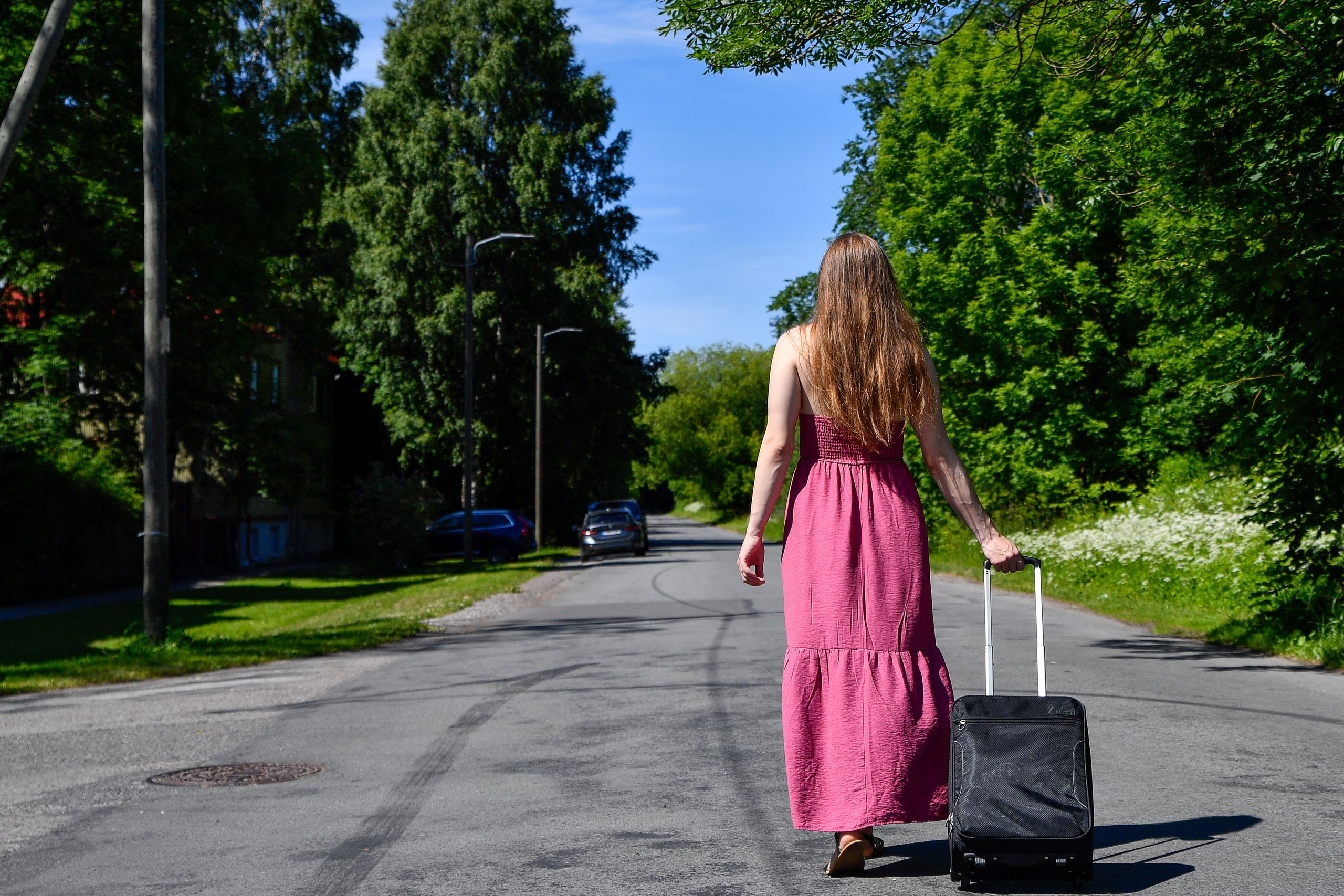 The Power of a Woman Walking Away - A woman in a pink dress walks down a sunny street in Tallinn, Estonia, pulling a suitcase.