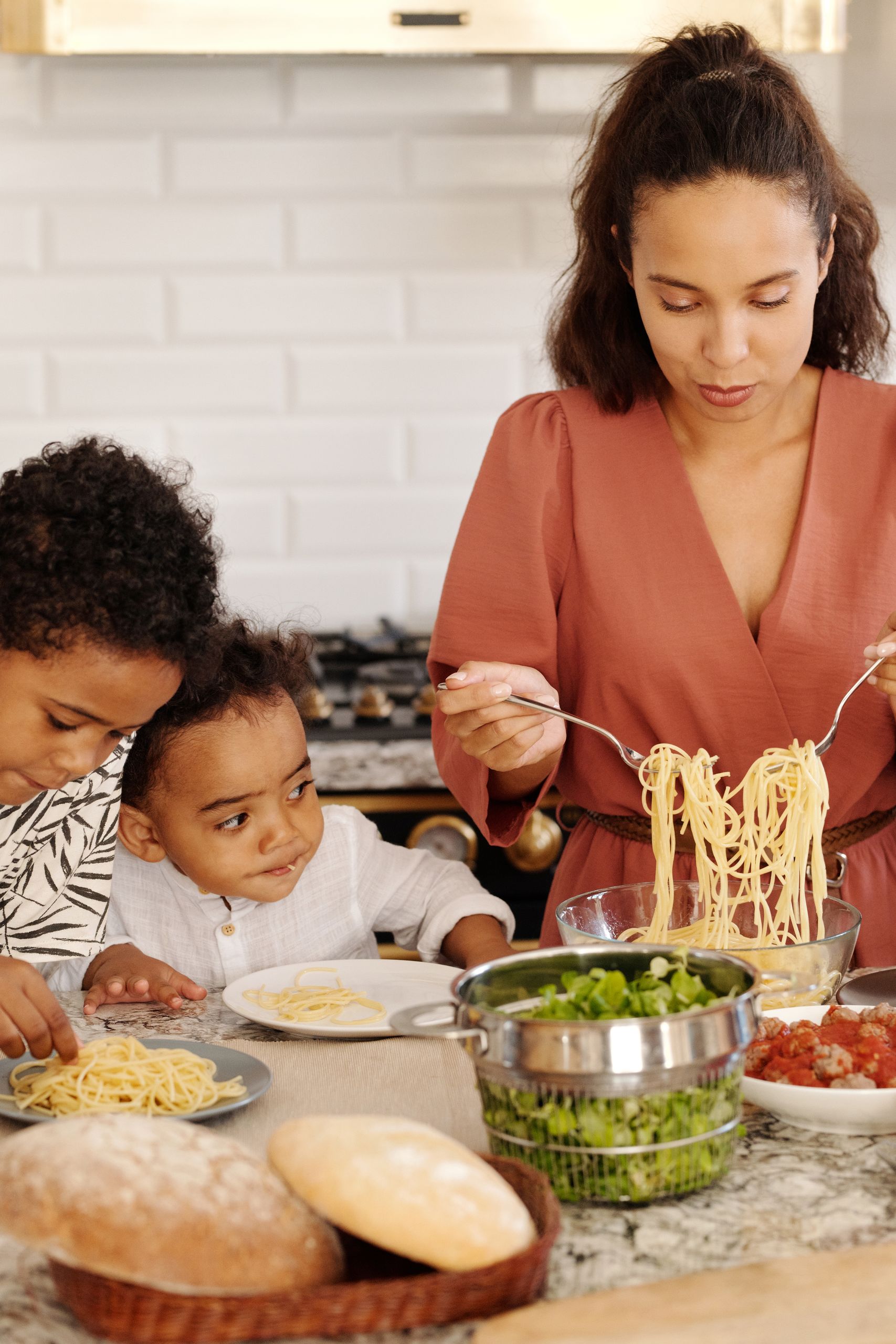 The Recipe Is Only Half the Family Story - A mother prepares pasta with her children in a modern kitchen, creating a warm family moment indoors.