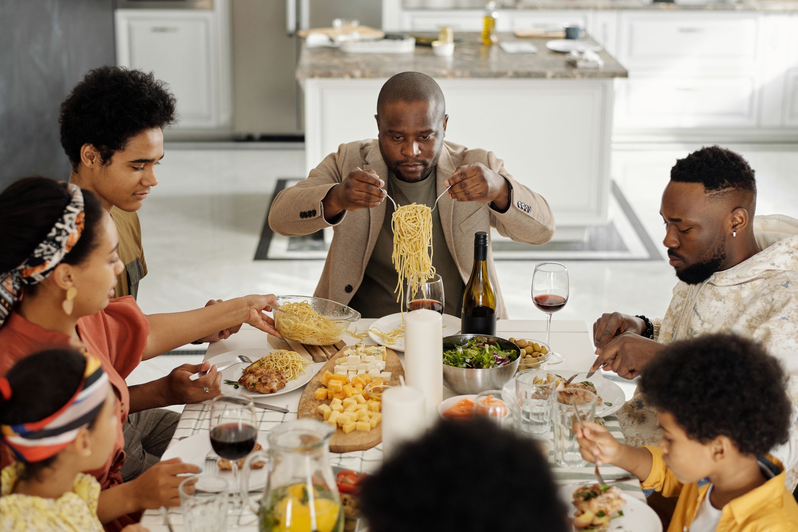 The Table Is Where I Learn People Best - A warm family gathering enjoying dinner together with wine and pasta.