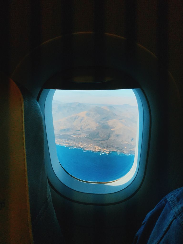 The Trip I Take Before I Leave - A breathtaking view of blue ocean and mountains from an airplane window.