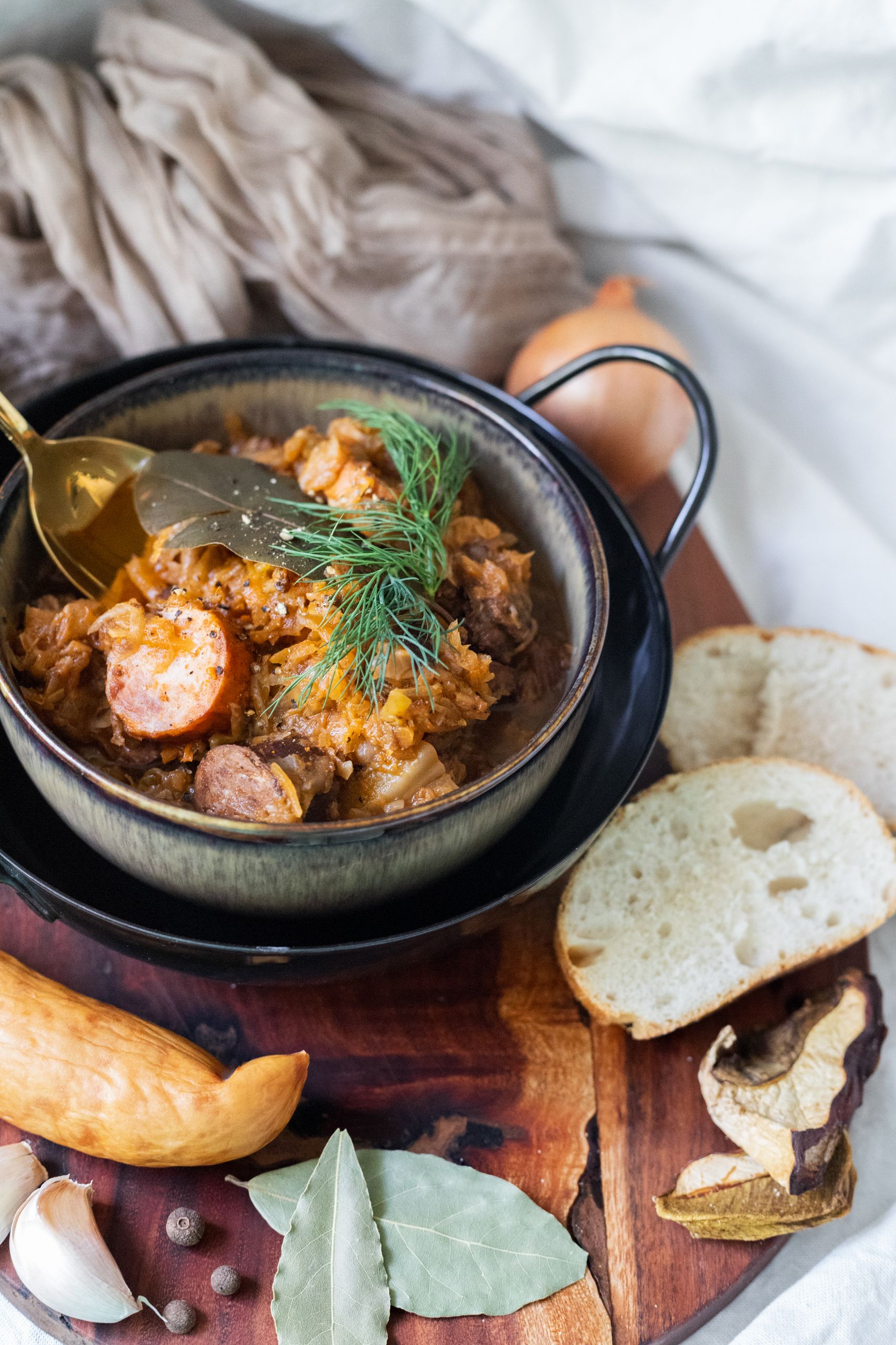 The Winter Meal That Helps Me Slow Down - Delicious bowl of traditional sauerkraut stew with sausage, garnished with dill, served with bread and spices.