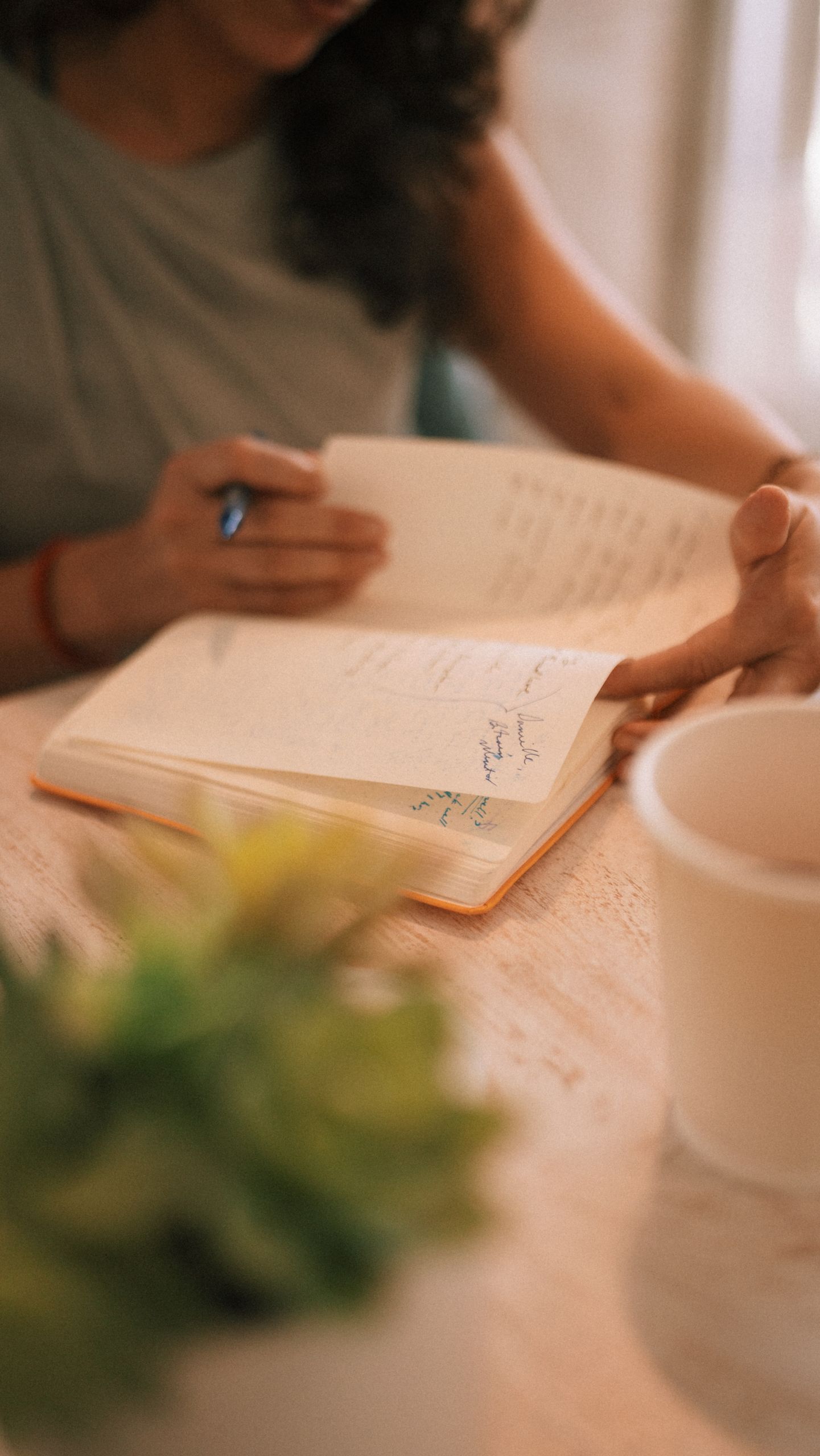 The Year I Want My Choices to Feel More Honest - Close-up of a person writing in a notebook with a coffee cup nearby, warm setting.