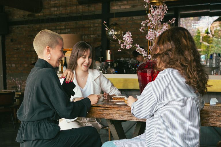 Women Taking Up Public Space Changes the Room - Three women laughing and enjoying dessert together in a cozy café setting.