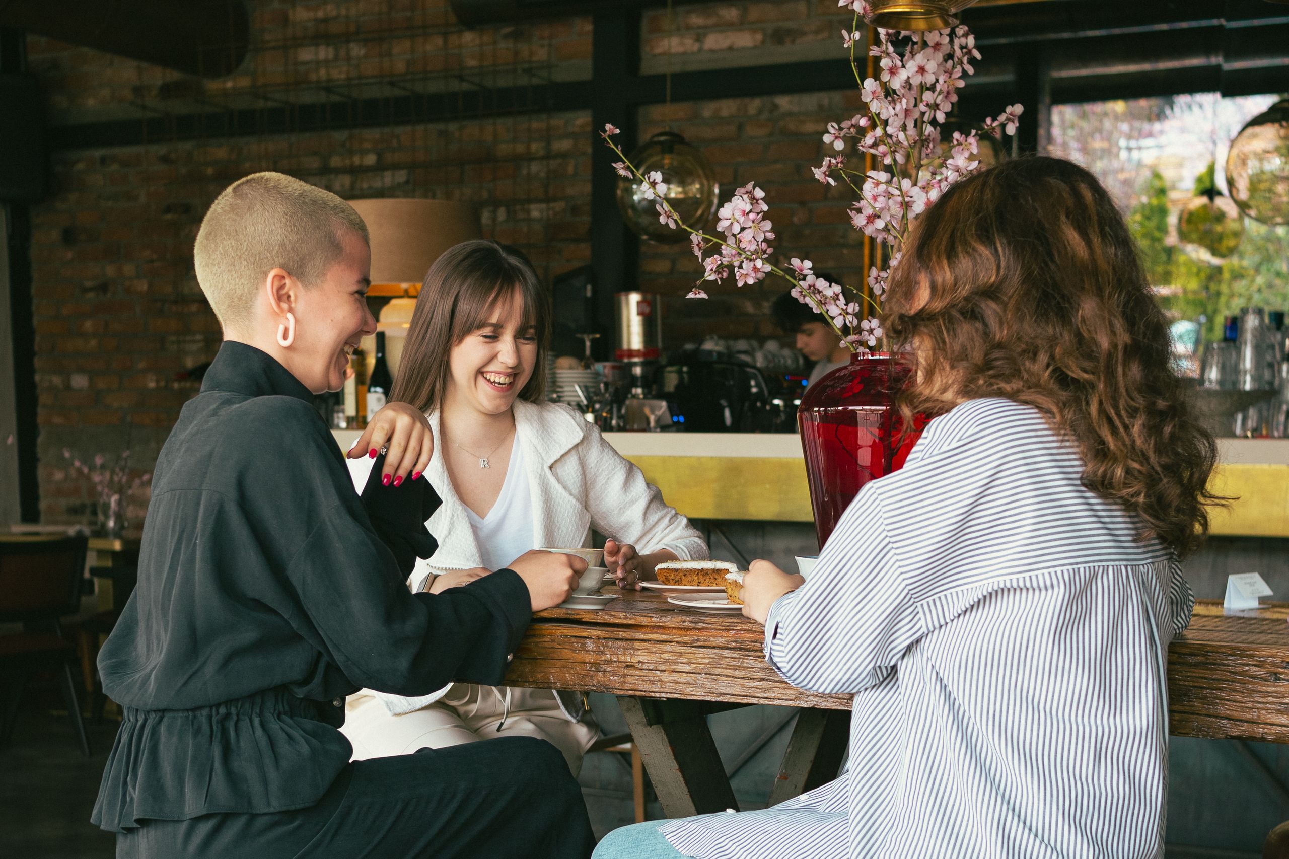 Women Taking Up Public Space Changes the Room - Three women laughing and enjoying dessert together in a cozy café setting.