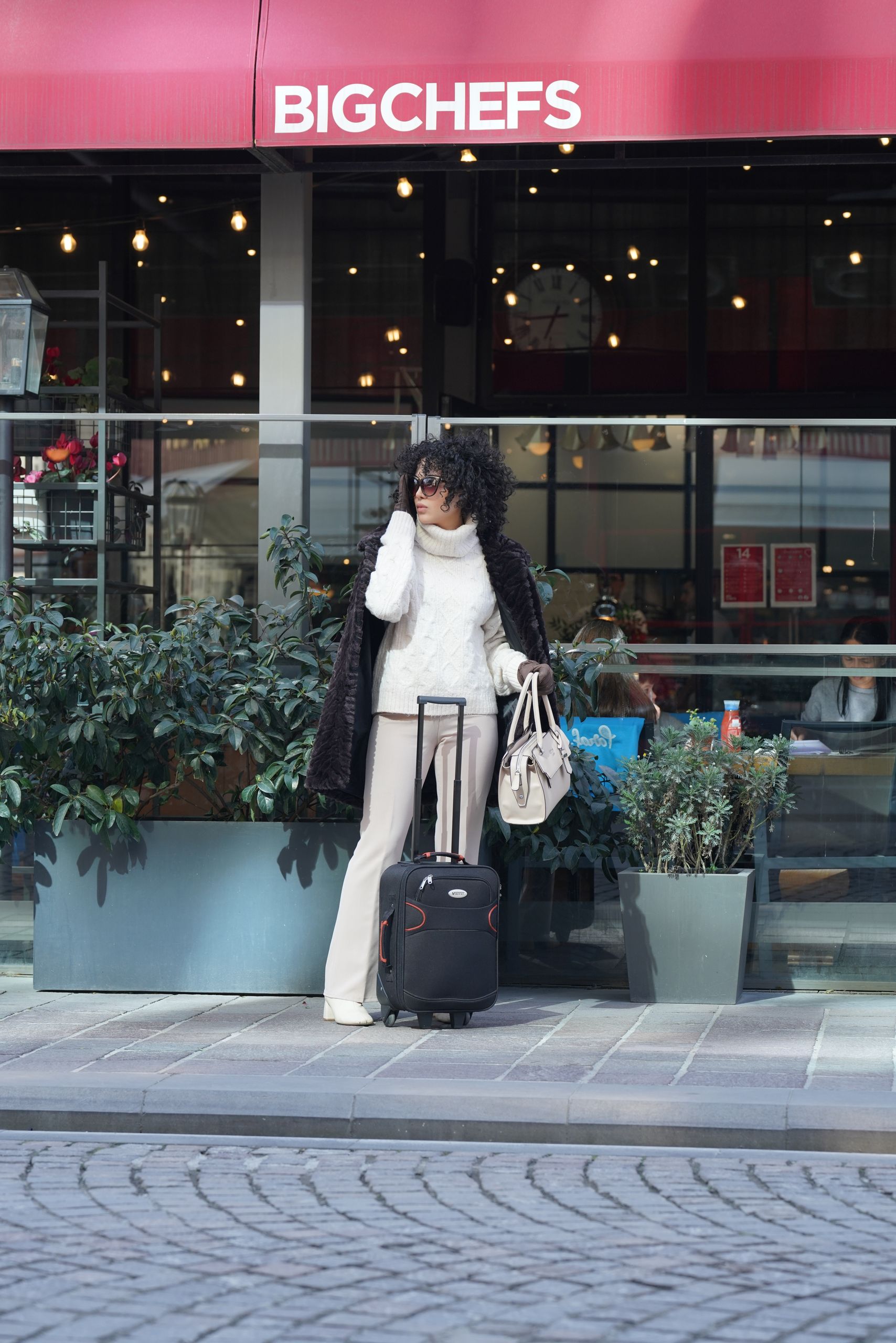 Travel Style - Fashionable woman with luggage outside BigChefs in Istanbul, capturing a chic urban moment.