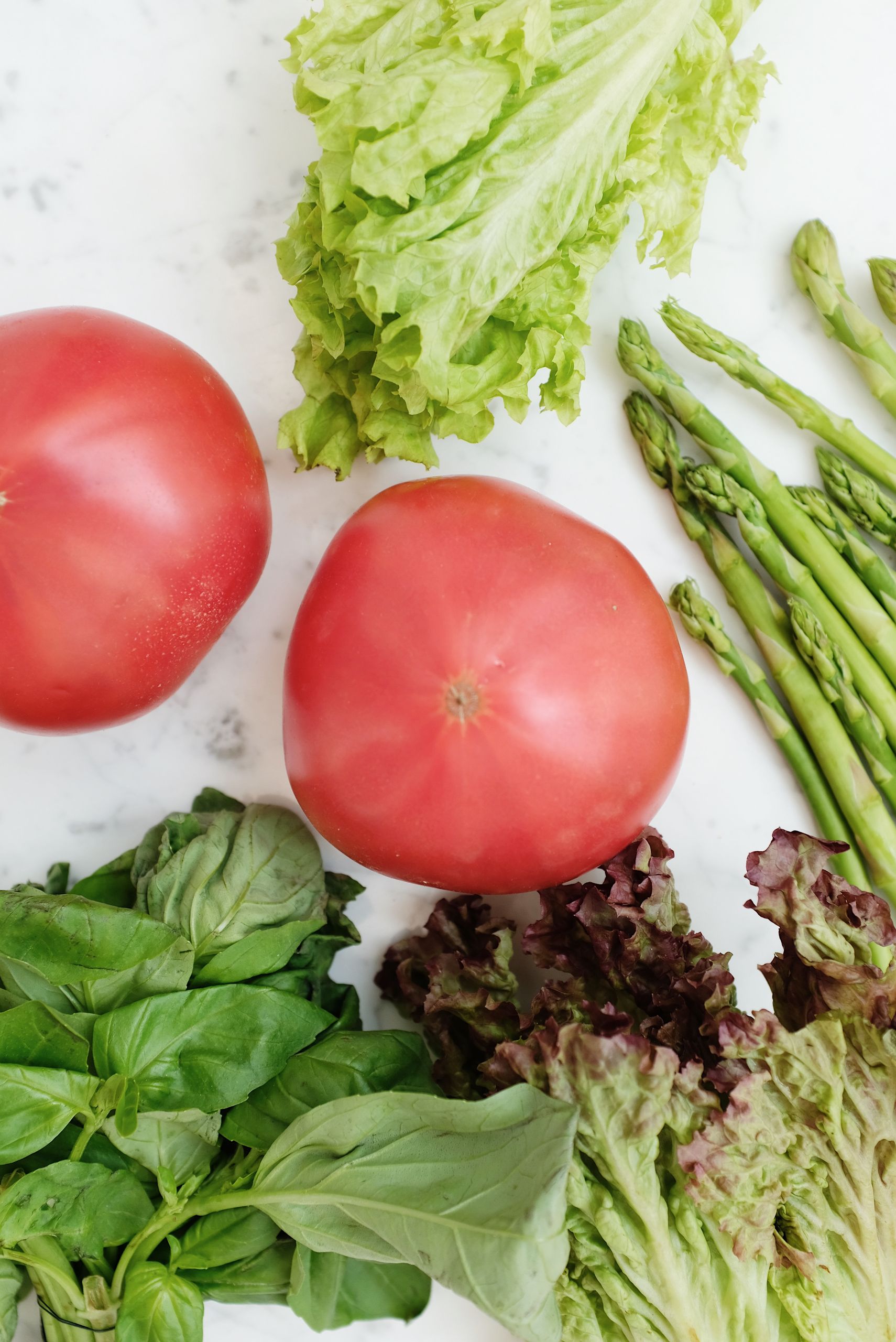 Vibrant assortment of fresh vegetables, including tomatoes, lettuce, and asparagus on a white background.